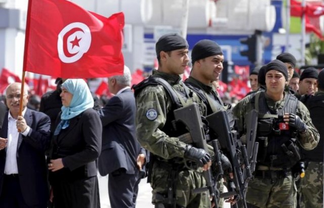 Tunisian security forces stand guard as Tunisians wave their national flag during a march against extremism outside Tunis' Bardo Museum