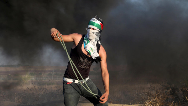 Masked Palestinian protester uses a sling to throw stones at Israeli troops during clashes near the border between Israel and Central Gaza Strip