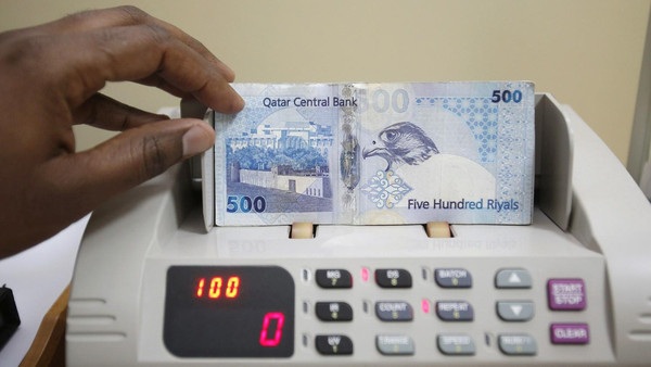 A cashier counts Qatari riyal notes at a money changer in Doha